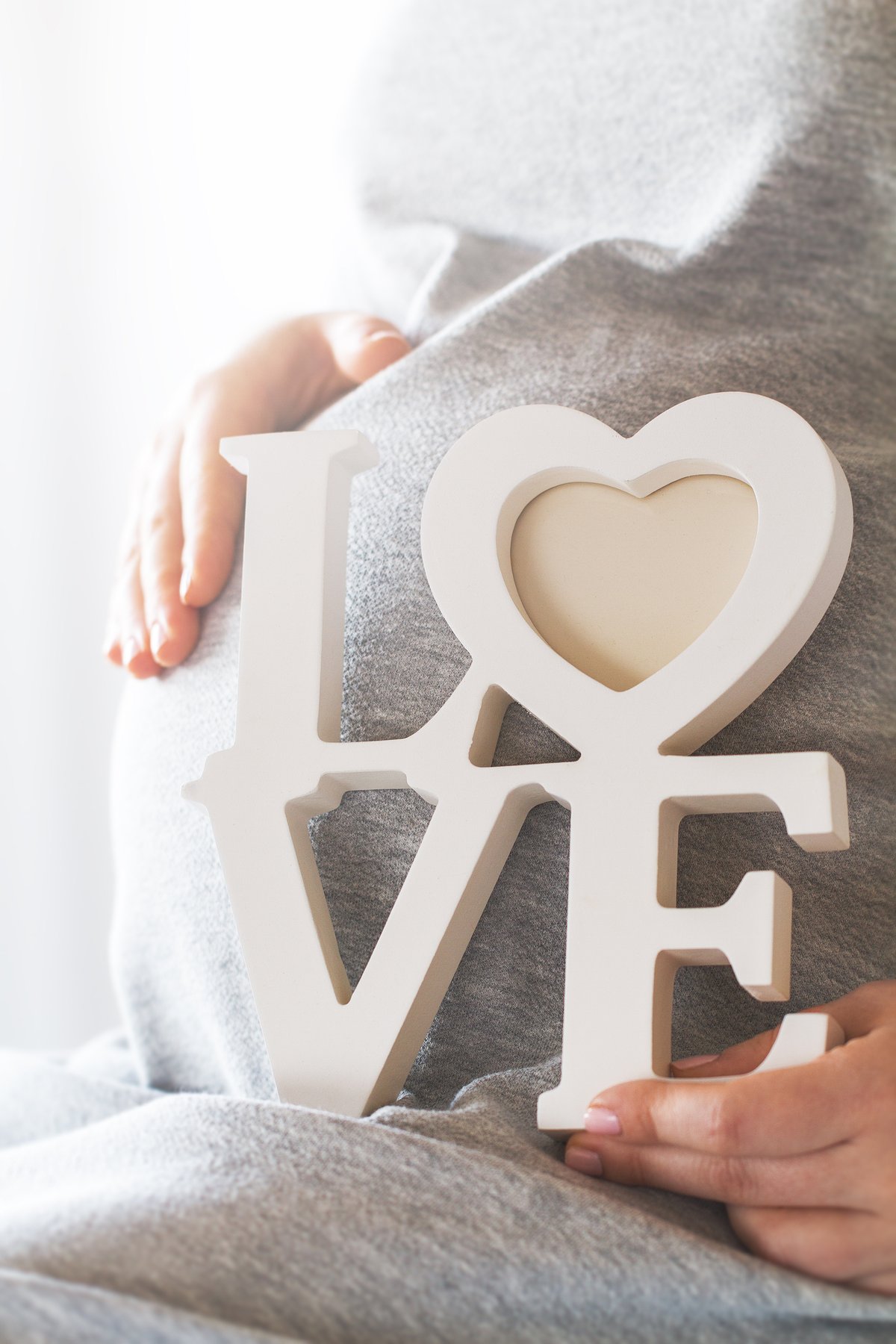 Hände formen ein Herz vor einem Babybauch — Symbol für Selbstliebe und Bindung in der Schwangerschaft